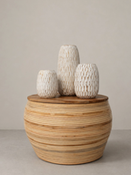 AYOMI GILI set of three white whitewashed hand-carved balsa wood vases with organic textures on a rattan base.
