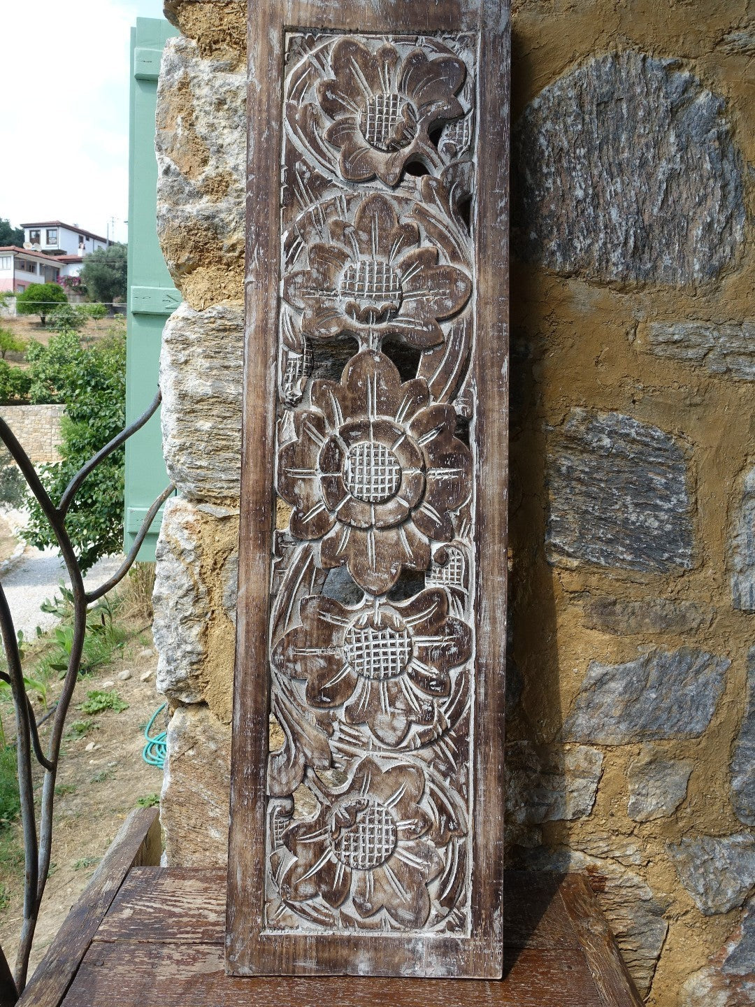 AYOMI Sakura ahşap oyma kahverengi duvar dekoru, çiçek motifli 100x27 cm. Taş duvarlı bir evde duvarda.